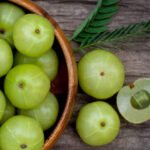 A glass of fresh amla juice with Indian gooseberries on a wooden table