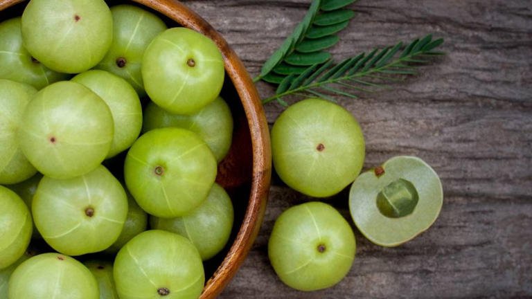 A glass of fresh amla juice with Indian gooseberries on a wooden table