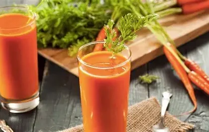 Glass of fresh carrot juice placed beside raw carrots on a wooden table