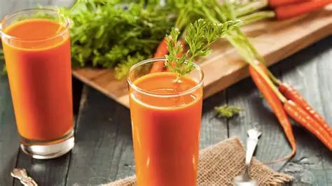 Glass of fresh carrot juice placed beside raw carrots on a wooden table